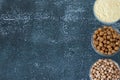 Chickpea (gram) flour, raw and cooked garbanzo beans in three bowls isolated on dark rustic table, copy space, top view