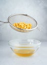 Chickpea water aquafaba. Egg replacement. Vegan concept. Metal sieve draining aquafaba chickpea water into glass bowl. on a gray