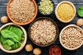 Chickpeas, lentils, peas, brown rice, bulgur, nuts and spinach on black rustic background. Various cereals and legumes. Vegetarian