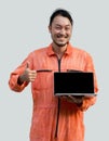 The chief mechanic in an orange uniform holding blank screen laptop computer. Standing with his finger thumbs up. Portrait with