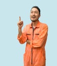 The chief mechanic in an orange uniform pointing one finger in upward direction. Portrait on blue background with studio light