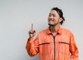 The chief mechanic in an orange uniform pointing one finger in upward direction. Portrait on gray background with studio light