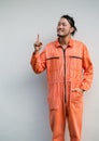 The chief mechanic in an orange uniform pointing one finger in upward direction. Portrait on gray background with studio light