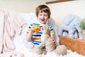 Chihuahua dog licks little laughing child`s face on couch with blanket. Portrait of a happy caucasian kid boy eat apple Royalty Free Stock Photo