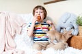 Chihuahua dog licks little laughing child`s face on couch with blanket. Portrait of a happy caucasian kid boy eat apple hugging a Royalty Free Stock Photo