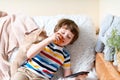 Chihuahua dog licks little laughing child`s face on couch with blanket. Portrait of a happy kid boy eat apple hugging a puppy at Royalty Free Stock Photo