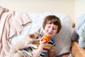 Chihuahua dog licks little laughing child& x27;s face on couch with blanket. Portrait of a happy caucasian kid boy eat apple Royalty Free Stock Photo