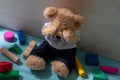Teddy bear covering eyes sitting on the floor colorful wooden blocks around