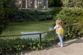 A child admires a small pond with fish in the park. A little girl with ponytails is leaning on the railing at the edge