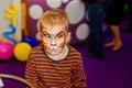 Child animator, artist`s hand draws face painting to little boy. Child with funny face painting. Painter makes orange tiger at bo