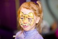 Child animator, artist`s hand draws face painting to little girl. Child with funny face painting. Painter makes yellow leopard at Royalty Free Stock Photo