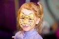 Child animator, artist`s hand draws face painting to little girl. Child with funny face painting. Painter makes yellow leopard at Royalty Free Stock Photo