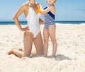 Child applying sunscreen on smiling mother in swimsuit at beach