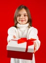 Child with arms extended forward holding gift box with red ribbon and bow. Kid looking at camera on red background Royalty Free Stock Photo