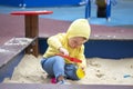 Child baby girl boy one year old playing on the playground in the sandbox. European Caucasian baby in yellow clothes plays in