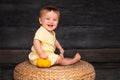 Child with the baby pumpkin smiling on the straw table on the wooden background