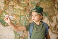 A child with a backpack on his back launches a paper plane into the air. The boy looks ahead confidently. World map background and