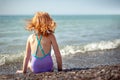 Child in a bathing suit sits on the beach and dreams