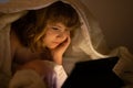 Child in bed under a blanket plays on a tablet in a game in the dark. The child face is illuminated by a tablet. Child Royalty Free Stock Photo