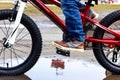 Child on a bike. Children`s foot on a bicycle pedal. Children`s bike in a puddle. The boy`s foot turns the bicycle pedal