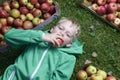 Child blond boy lying on the green grass with apples background, holding, eating and biting apple Royalty Free Stock Photo