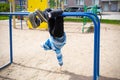 Child in blue jacket hanging on crossbars upside down in playground, against backdrop of house and cars Royalty Free Stock Photo