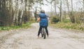 Child in blue vest and black leggings rides balance bike on dirt road, in countryside Royalty Free Stock Photo