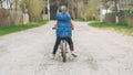 Child in blue vest and black leggings rides balance bike on dirt road, in countryside Royalty Free Stock Photo
