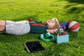 Child with book and taplet and resting on the grass after school. Happy boy relaxing on the grass. Royalty Free Stock Photo