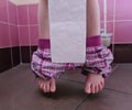 Child with bowel problems and constipation holds toilet paper sitting on toilet