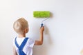 Child boy Builder paints white walls with a roller in an apartment, a child makes house repairs, rear view, place for text Royalty Free Stock Photo