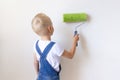 Child boy Builder paints white walls with a roller in an apartment, a child makes house repairs, rear view, place for text Royalty Free Stock Photo