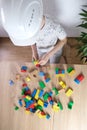 Child, a boy in a builder`s helmet plays with colored wooden cubes, builds houses and rockets, the concept of the development of