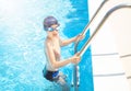 Child (boy) is on ladder handrails (stairs) in to the swimming pool smiling after swimming.