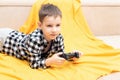 The child boy in checked shirt lying on the couch with black joystick in his hands playing the video game. Playing video Royalty Free Stock Photo