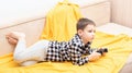The child boy in checked shirt lying on the couch with black joystick in his hands playing the video game. Playing video Royalty Free Stock Photo