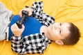 The child boy in checked shirt lying on the couch with black joystick in his hands playing the video game. Playing video Royalty Free Stock Photo