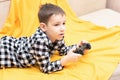 The child boy in checked shirt lying on the couch with black joystick in his hands playing the video game. Playing video Royalty Free Stock Photo