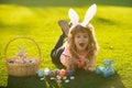 Child boy with easter eggs and bunny ears painting eggs outdoor. Cute kid having happy easter in park. Royalty Free Stock Photo