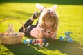 Child boy with easter eggs and bunny ears painting eggs outdoor. Cute kid having happy easter in park. Royalty Free Stock Photo