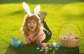 Child boy with easter eggs and bunny ears painting eggs outdoor. Cute kid having happy easter in park. Royalty Free Stock Photo