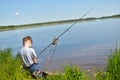 Boy child fisherman sits on shore and looks at float. Fishing with children Royalty Free Stock Photo