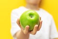 Child boy giving green fresh aplle on cheerful yellow background. Blurred figure of the kid. Focus on apple