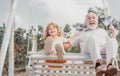 Child boy and grandfather swinging in summer garden. Grand dad and grandson sitting on swing in park. Generations ages. Royalty Free Stock Photo
