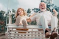 Child boy and grandfather swinging in summer garden. Grand dad and grandson sitting on swing in park. Generations ages. Royalty Free Stock Photo