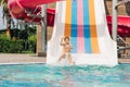 Child boy laughing while slide in pool after going down water slide at sunny day in water Aqua park. Kid refreshing at Royalty Free Stock Photo