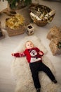 Child boy is lying on the carpet next to the festive garlands and gift boxes.