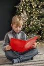 Child boy opens magic book, reads Christmas stories and fairy tales. Concept Merry Christmas