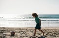 Child boy play football on sand beach.