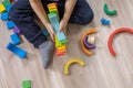 Child boy playing colored rainbow wooden Montessori material arch spectrum row at home floor